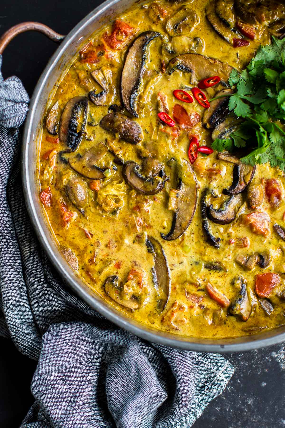 Baked Mushroom Curry in a copper pan with a tea towel resting underneath.