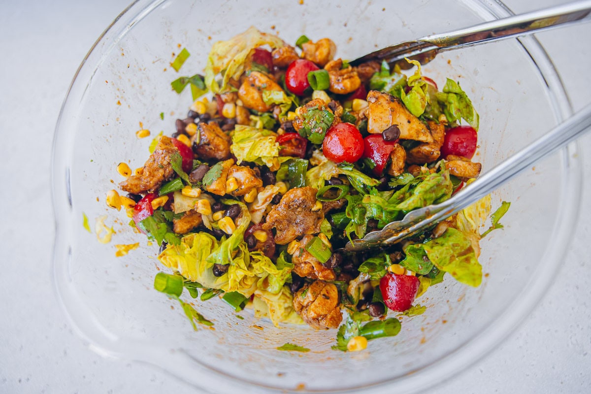 Mexican Chicken Salad and dressing being mixed in a bowl with tongs. 